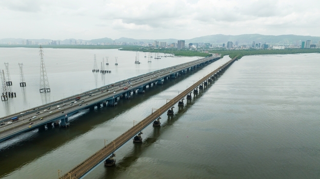 Aerial view of Vashi Bridge with traffic and the adjacent railway bridge spanning the creek featuring power pylons and the city skyline in Navi Mumbai Maharashtra India.