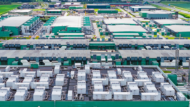 Aerial view of a large industrial data center facility featuring numerous cooling units on the roof and expansive green warehouse buildings in Middenmeer North Holland Netherlands.