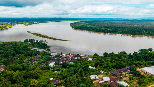 Aerial view of the Cross River flowing past the village of Itu surrounded by lush tropical vegetation and palm trees under a cloudy sky in Itu Akwa Ibom Nigeria. Aerial view of the Cross River flowing past the village of Itu surrounded by lush tropical vegetation and palm trees under a cloudy sky in Itu Akwa Ibom Nigeria.