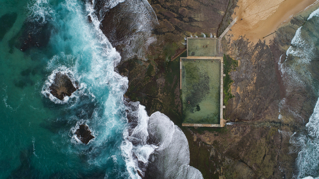 Aerial view of Newport Rock Pool with turquoise waves crashing against the rocky shore and white foam in Sydney New South Wales Australia.