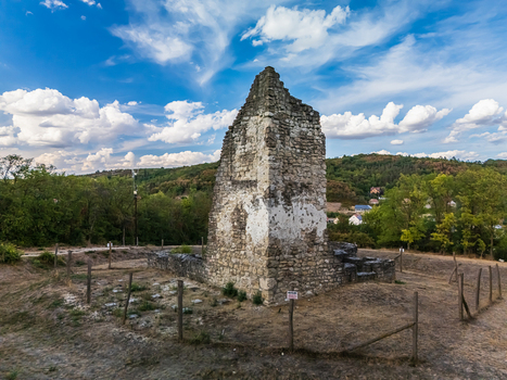 Aerial view of medieval stone church ruins in Csabdi Hungary rising above a wooded rural valley with scattered houses under a blue sky and drifting clouds. Aerial view of medieval stone church ruins in Csabdi Hungary rising above a wooded rural valley with scattered houses under a blue sky and drifting clouds.
