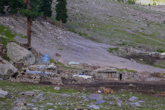 View of traditional stone huts with smoke rising from a chimney in the rugged landscape of Rama Meadows Astore Gilgit Pakistan. View of traditional stone huts with smoke rising from a chimney in the rugged landscape of Rama Meadows Astore Gilgit Pakistan.