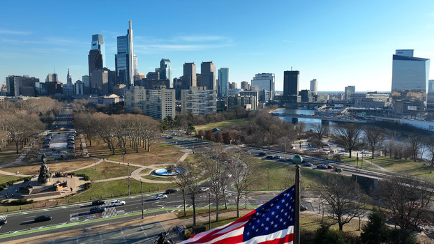 Aerial view of the Philadelphia skyline with an American flag in the foreground urban buildings the Schuylkill River and park spaces in Philadelphia Pennsylvania United States.