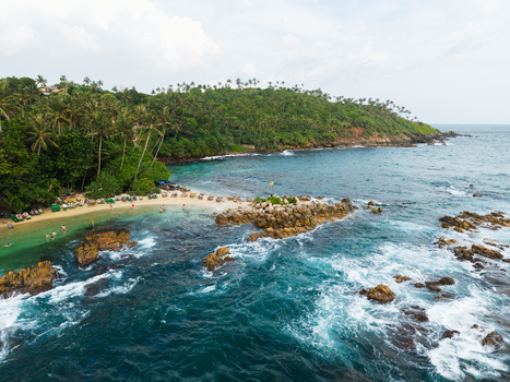 Aerial view of Secret Beach Mirissa with turquoise waves crashing against rocky outcrops and people relaxing on the sandy shore in Mirissa Southern Province Sri Lanka. Aerial view of Secret Beach Mirissa with turquoise waves crashing against rocky outcrops and people relaxing on the sandy shore in Mirissa Southern Province Sri Lanka.