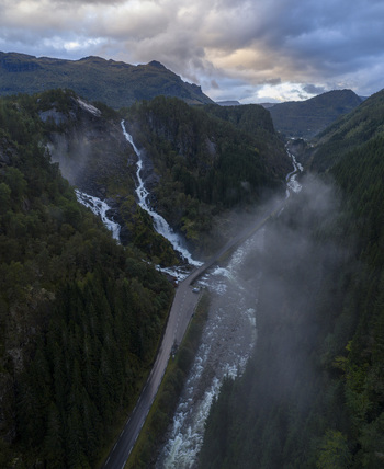 Aerial view of Latefossen waterfall cascading down rocky cliffs into a river valley with mist and lush forests Skare Vestland Norway.