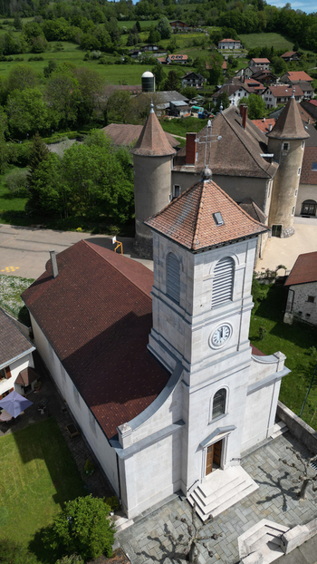 Aerial view of Chateau De Vesancy and the village church with its stone clock tower surrounded by lush green hills in Vesancy Auvergne Rhone Alpes France. Aerial view of Chateau De Vesancy and the village church with its stone clock tower surrounded by lush green hills in Vesancy Auvergne Rhone Alpes France.