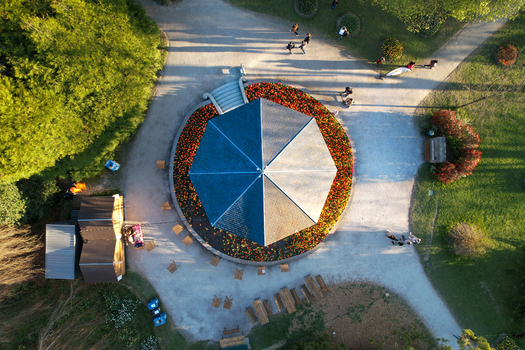 Aerial view of a circular pavilion with a blue and white roof surrounded by vibrant flower beds and people walking on gravel paths in a park Morges Vaud Switzerland. Aerial view of a circular pavilion with a blue and white roof surrounded by vibrant flower beds and people walking on gravel paths in a park Morges Vaud Switzerland.