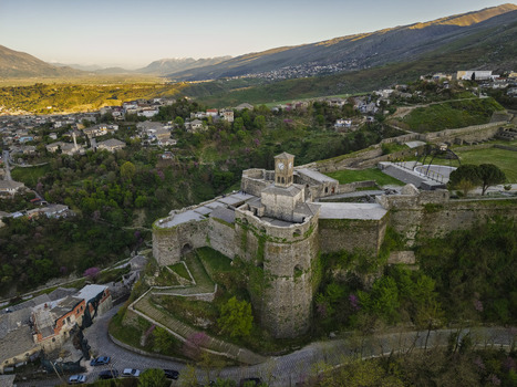 Aerial view of Gjirokaster Fortress with its clock tower and stone walls overlooking the historic town and lush mountain landscape in Gjirokaster Gjirokaster County Albania. Aerial view of Gjirokaster Fortress with its clock tower and stone walls overlooking the historic town and lush mountain landscape in Gjirokaster Gjirokaster County Albania.