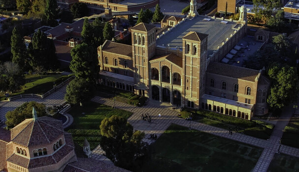 Aerial view of the historic Royce Hall on the UCLA campus featuring its iconic twin towers red tiled roof and the surrounding paved courtyard with students Westwood California United States.