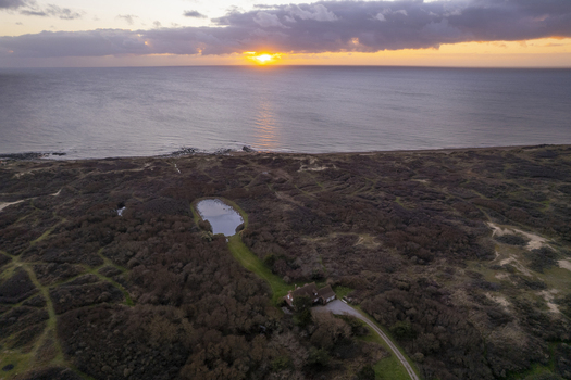 Aerial view of a house near a small pond and coastal dunes overlooking the sea at sunset in Audresselles Hauts de France France.
