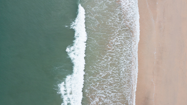 Aerial view of turquoise waves crashing onto the golden sand of Harlyn Bay Beach in Saint Merryn Cornwall United Kingdom.