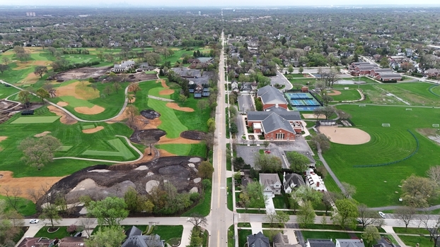 Aerial view of a straight road dividing a lush green golf course from a residential neighborhood with sports fields and tennis courts in Chicago Illinois United States.