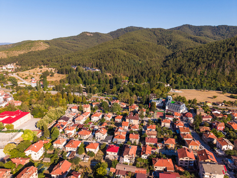 Aerial view of the town of Velingrad nestled in a valley surrounded by lush green forested mountains with red roofed houses and clear blue sky in Velingrad Pazardzhik Bulgaria. Aerial view of the town of Velingrad nestled in a valley surrounded by lush green forested mountains with red roofed houses and clear blue sky in Velingrad Pazardzhik Bulgaria.
