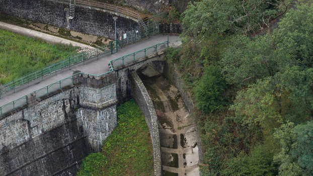 Aerial view of Sengbachtalsperre dam structure featuring a stone bridge concrete spillway and surrounding lush forest in Solingen Nordrhein Westfalen Germany. Aerial view of Sengbachtalsperre dam structure featuring a stone bridge concrete spillway and surrounding lush forest in Solingen Nordrhein Westfalen Germany.