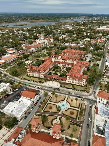 Aerial view of Flagler College featuring red tiled roofs and Spanish Renaissance architecture with lush courtyards and palm trees in St. Augustine Florida United States.