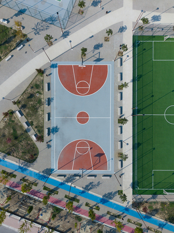 Aerial view of a modern sports park featuring a basketball court with red and blue markings next to a green soccer field surrounded by paved walkways in Berat Berat County Albania.