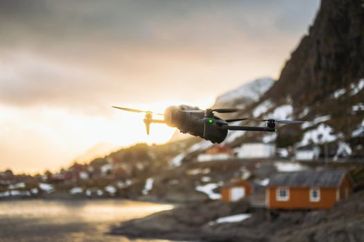 View of a drone in flight over the serene Lofoten Islands with snow capped mountains rustic cabins and a tranquil body of water Tind Nordland Norway.