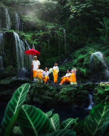 Bali Indonesia View of a ceremonial gathering by a cascading waterfall where vibrant orange fabrics contrast with the lush green foliage and cool misty air. Bali Indonesia View of a ceremonial gathering by a cascading waterfall where vibrant orange fabrics contrast with the lush green foliage and cool misty air.