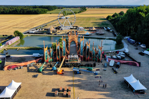 Herzogenaurach Germany 22 July 2022 Aerial view of the Open Beatz Festival setup featuring a large main stage a Ferris wheel and surrounding golden fields under a clear sky. Herzogenaurach Germany 22 July 2022 Aerial view of the Open Beatz Festival setup featuring a large main stage a Ferris wheel and surrounding golden fields under a clear sky.