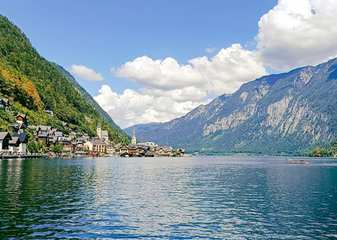 View of Hallstatt village nestled between the steep mountains and the calm waters of Lake Hallstatt under a bright blue sky with fluffy clouds Hallstatt Upper Austria Austria. View of Hallstatt village nestled between the steep mountains and the calm waters of Lake Hallstatt under a bright blue sky with fluffy clouds Hallstatt Upper Austria Austria.