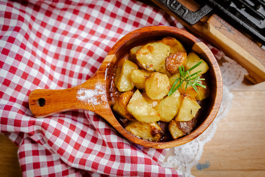 View of golden roasted potatoes nestled in a wooden bowl sprinkled with salt and a sprig of rosemary against a red and white checkered cloth Pula Croatia.