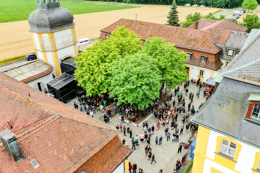 Aerial view of Schloss Jagersburg featuring a crowd of people gathered in the courtyard surrounded by historic buildings and lush green trees in Eggolsheim Bayern Germany. Aerial view of Schloss Jagersburg featuring a crowd of people gathered in the courtyard surrounded by historic buildings and lush green trees in Eggolsheim Bayern Germany.
