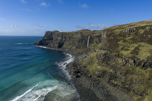 Aerial view of Talisker Bay Beach with its dramatic cliffs and a waterfall plunging into the Atlantic Ocean under a clear blue sky Isle of Skye Scotland United Kingdom. Aerial view of Talisker Bay Beach with its dramatic cliffs and a waterfall plunging into the Atlantic Ocean under a clear blue sky Isle of Skye Scotland United Kingdom.