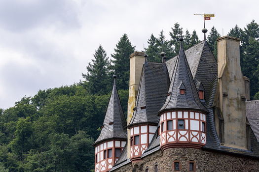 View of the medieval towers of Eltz Castle with half timbered walls and pointed slate roofs against a backdrop of dense green forest in Wierschem Rhineland Palatinate Germany.