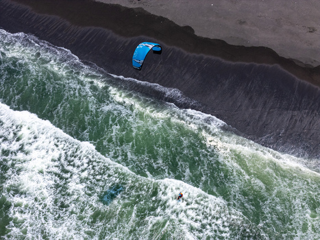 Aerial view of a kitesurfer riding waves along the black sand shore of Depok Beach in the Special Region of Yogyakarta Indonesia.