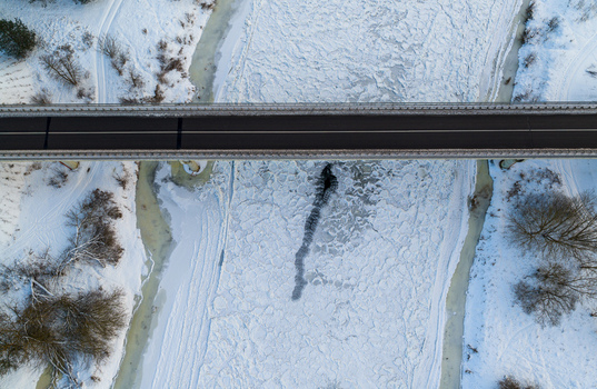 Aerial view of a bridge crossing a frozen river covered in ice floes and snow covered banks in Lithuania. Aerial view of a bridge crossing a frozen river covered in ice floes and snow covered banks in Lithuania.