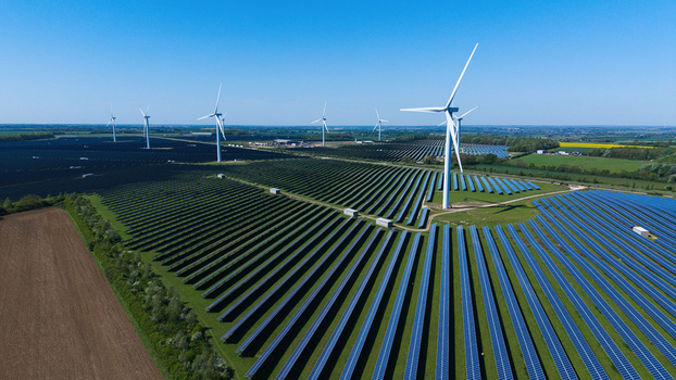 Aerial view of Chelveston Wind Farm featuring rows of solar panels and tall wind turbines under a clear blue sky in Wellingborough England United Kingdom. Aerial view of Chelveston Wind Farm featuring rows of solar panels and tall wind turbines under a clear blue sky in Wellingborough England United Kingdom.