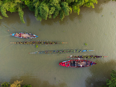 Aerial view of vibrant boats cutting through the murky river waters under a dense canopy of trees Gopalganj Dhaka Division Bangladesh. Aerial view of vibrant boats cutting through the murky river waters under a dense canopy of trees Gopalganj Dhaka Division Bangladesh.