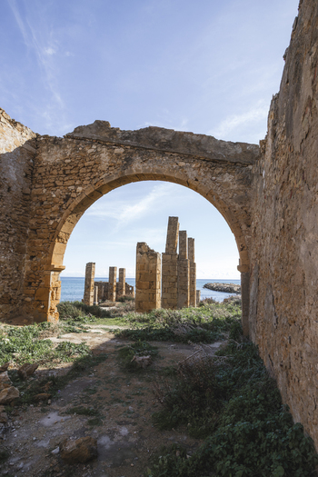 View of the Tonnara di Avola ruins featuring a stone arch and pillars overlooking the Mediterranean Sea under a clear blue sky Avola Sicily Italy. View of the Tonnara di Avola ruins featuring a stone arch and pillars overlooking the Mediterranean Sea under a clear blue sky Avola Sicily Italy.