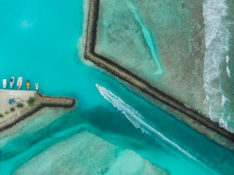 Aerial view of a boat cutting through the turquoise waters leaving a trail between the dark stone jetties Vashafaru Island Maldives. Aerial view of a boat cutting through the turquoise waters leaving a trail between the dark stone jetties Vashafaru Island Maldives.