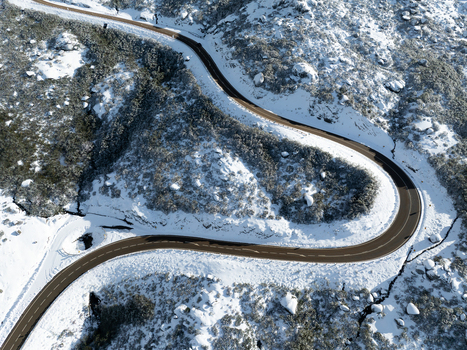 Aerial view of a winding asphalt road cutting through a snow dusted landscape the dark pavement contrasting with the surrounding white terrain São Romão Portugal. Aerial view of a winding asphalt road cutting through a snow dusted landscape the dark pavement contrasting with the surrounding white terrain São Romão Portugal.