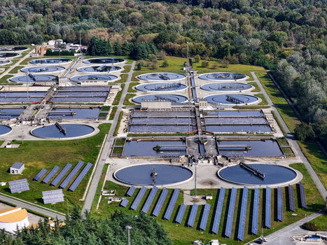 Aerial view of the Impianto depurazione water treatment plant featuring circular clarifiers and solar panels surrounded by lush forest in Castiglione Torinese Piedmont Italy.