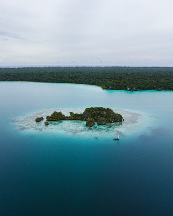 Aerial view of vivid turquoise waters meet a small forested island contrasting with the dark green mainland beyond Pine Island L Île des Pins New Caledonia. Aerial view of vivid turquoise waters meet a small forested island contrasting with the dark green mainland beyond Pine Island L Île des Pins New Caledonia.