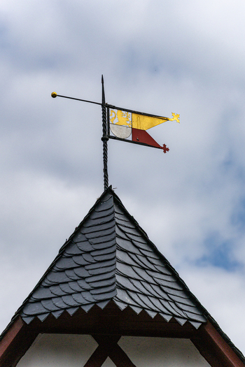 View of the heraldic weather vane atop a slate tiled roof spire of Eltz Castle against a cloudy sky in Wierschem Rhineland Palatinate Germany.