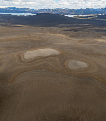 Aerial view of the volcanic landscape featuring unique circular soil patterns barren terrain distant snow capped mountains and a glacial lake in Iceland. Aerial view of the volcanic landscape featuring unique circular soil patterns barren terrain distant snow capped mountains and a glacial lake in Iceland.