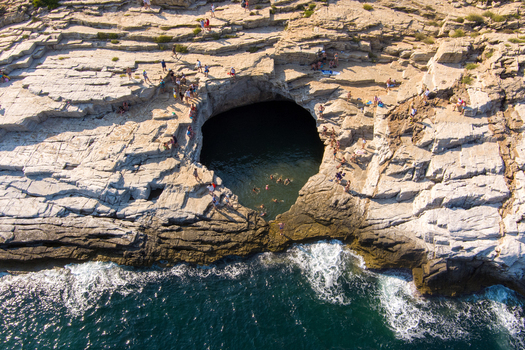 Greece 21 September 2026 Aerial view of Giola natural pool with people swimming in the clear turquoise water surrounded by rugged limestone cliffs on the coast of Thassos. Greece 21 September 2026 Aerial view of Giola natural pool with people swimming in the clear turquoise water surrounded by rugged limestone cliffs on the coast of Thassos.