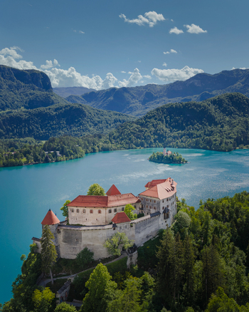 Aerial view of Bled Castle on a steep cliff overlooking the turquoise waters of Lake Bled and the island church surrounded by mountains at Bled Radovljica Slovenia.