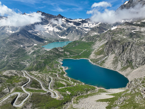 Aerial view of Agnel Lake and Serru Lake with the winding Colle del Nivolet road surrounded by snow capped peaks and green slopes Ceresole Reale Piedmont Italy.