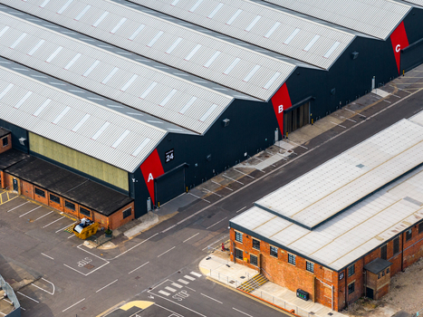 Aerial view of Ark Data Centres at Longcross Park featuring large industrial buildings with distinctive red marked entrances and metal roofs in Chertsey England United Kingdom. Aerial view of Ark Data Centres at Longcross Park featuring large industrial buildings with distinctive red marked entrances and metal roofs in Chertsey England United Kingdom.