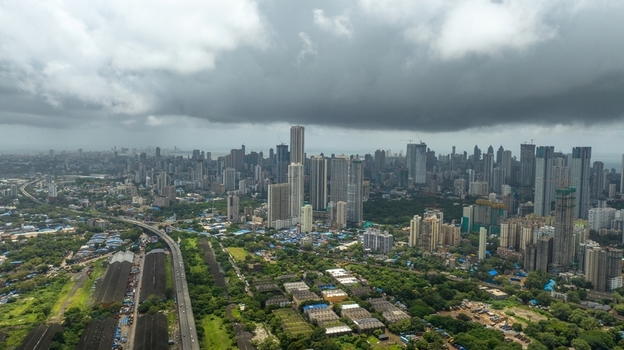 Aerial view of the Mumbai skyline featuring modern skyscrapers dense urban development and a highway under a dramatic cloudy sky in Mumbai Maharashtra India.