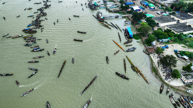 Baghabari Rajshahi Division Bangladesh 20 August 2022 Aerial view of traditional long boats navigating the river near the port with crowds gathered on the bank.