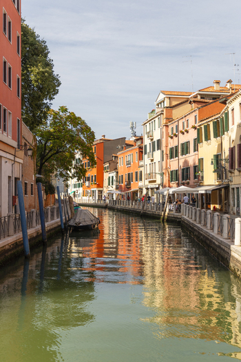 View of a quiet canal in Venice lined with historic colorful buildings a small moored boat and people walking along the waterfront in Venice Veneto Italy. View of a quiet canal in Venice lined with historic colorful buildings a small moored boat and people walking along the waterfront in Venice Veneto Italy.