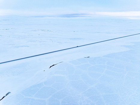 Aerial view of a lonely road cutting through a vast snow covered landscape under a bright sky in Egilsstadir Mulathing Iceland. Aerial view of a lonely road cutting through a vast snow covered landscape under a bright sky in Egilsstadir Mulathing Iceland.
