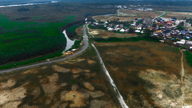 Aerial view of a winding road passing through a rural landscape with lush green vegetation a river and a small residential settlement in Rivers Nigeria.