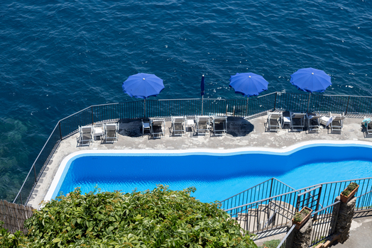 Aerial view of a swimming pool with blue umbrellas and lounge chairs overlooking the sea in Amalfi Campania Italy. Aerial view of a swimming pool with blue umbrellas and lounge chairs overlooking the sea in Amalfi Campania Italy.