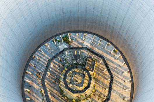 Aerial view of the interior of a massive concrete cooling tower featuring circular structural supports and long geometric shadows in Trino Piedmont Italy.